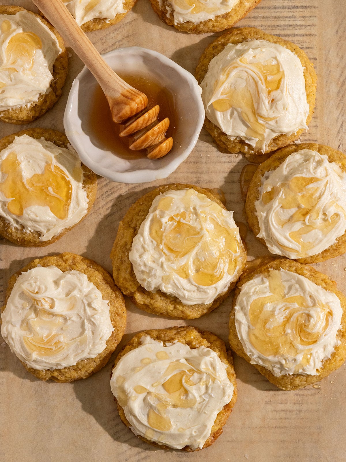 overhead view of parchment paper filled with cornmeal cookies topped with frosting, a drizzle of honey, and flaky sea salt.