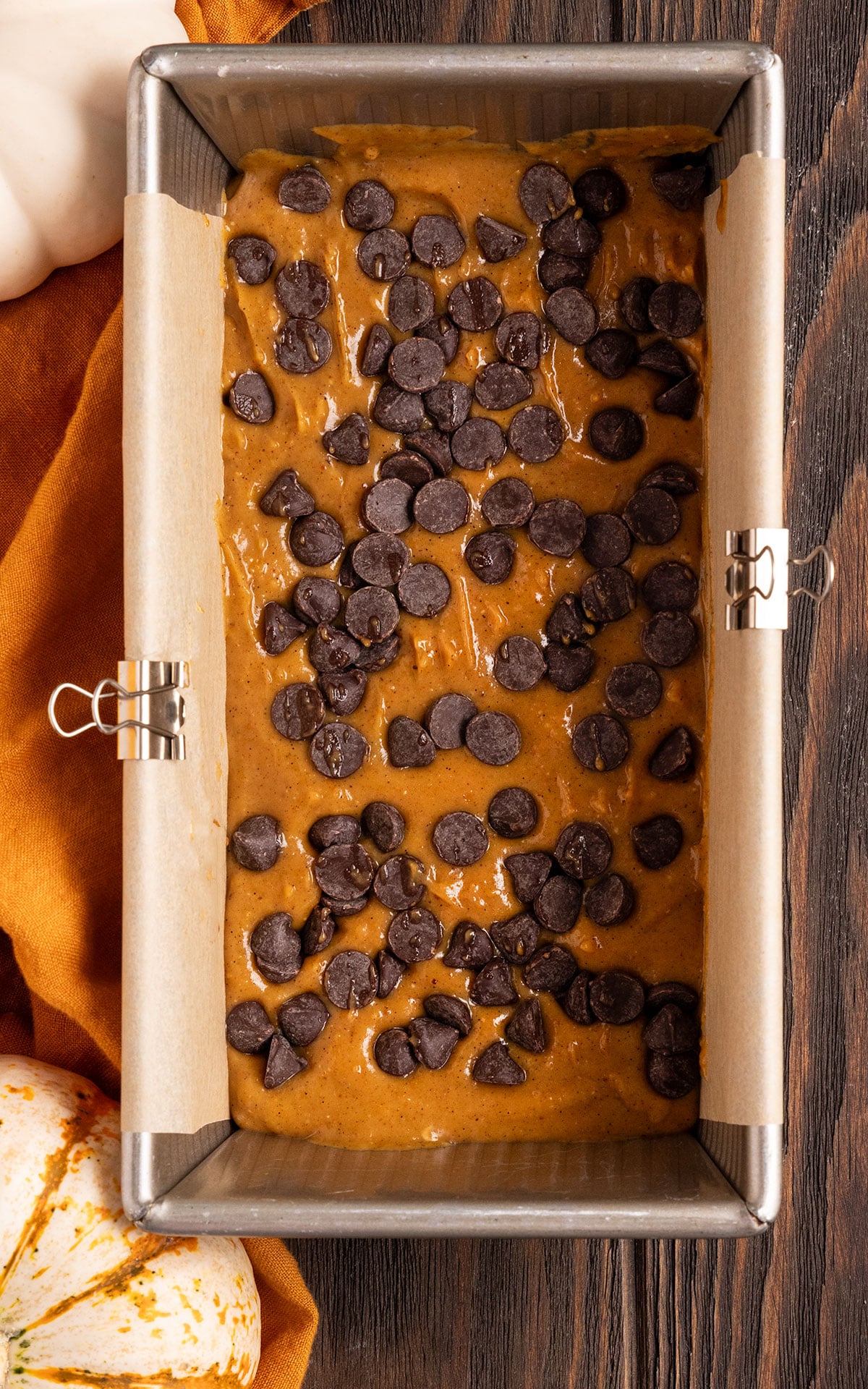 loaf pan filled with parchment paper with pumpkin fudge batter and chocolate chips inside.