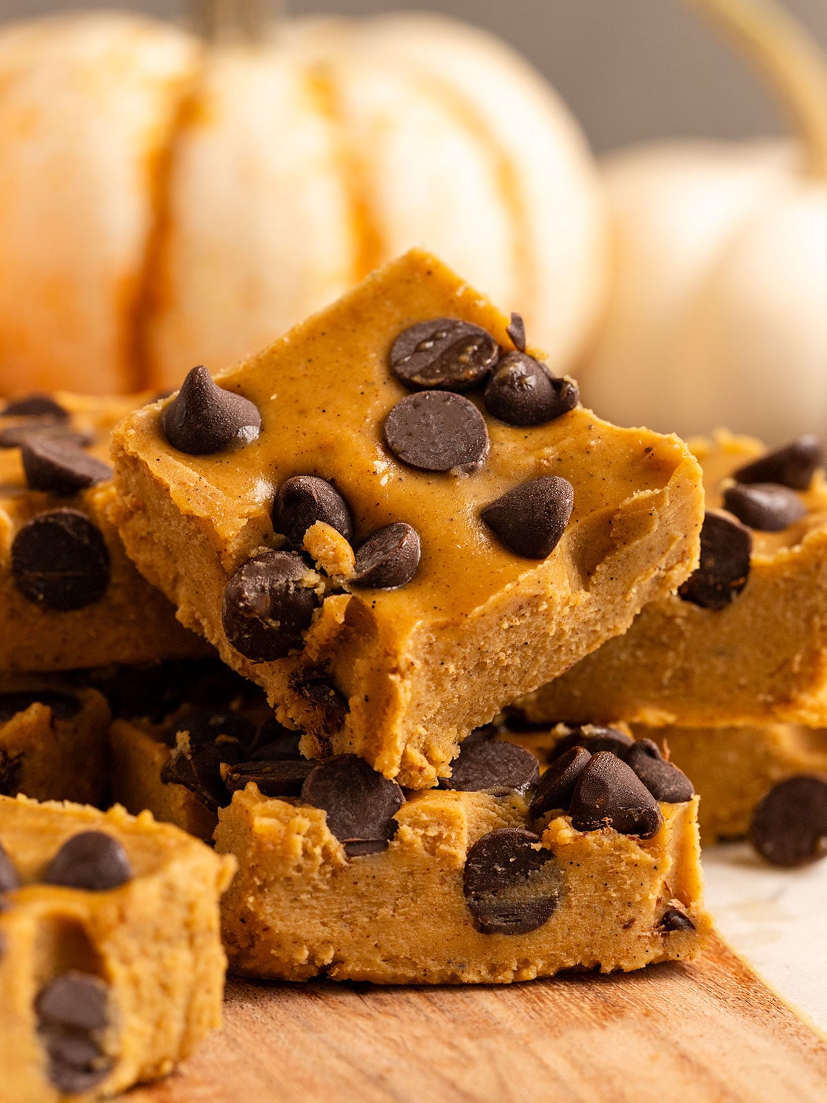 stacks of pumpkin fudge with chocolate chips in them in front of pumpkins.