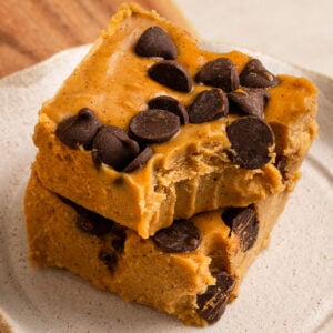 two slices of pumpkin fudge with chocolate chips stacked on a plate with the top square missing a bite.