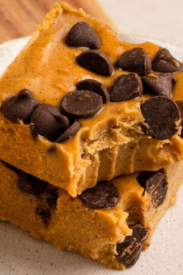 two slices of pumpkin fudge with chocolate chips stacked on a plate with the top square missing a bite.