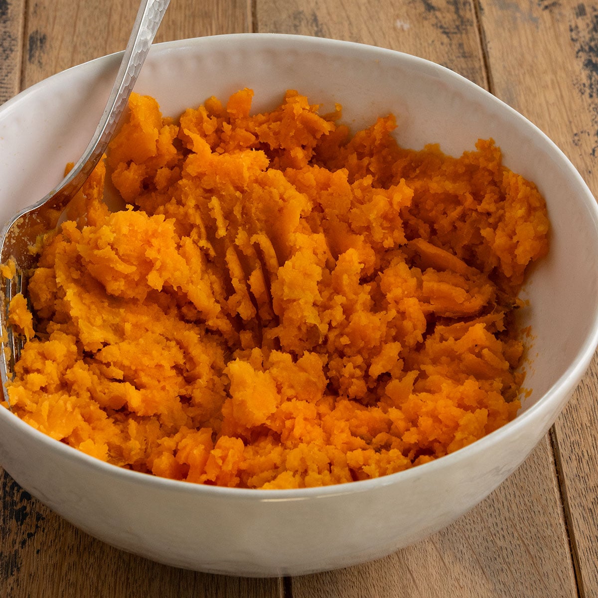 bowl of orange mashed sweet potato with a fork inside.