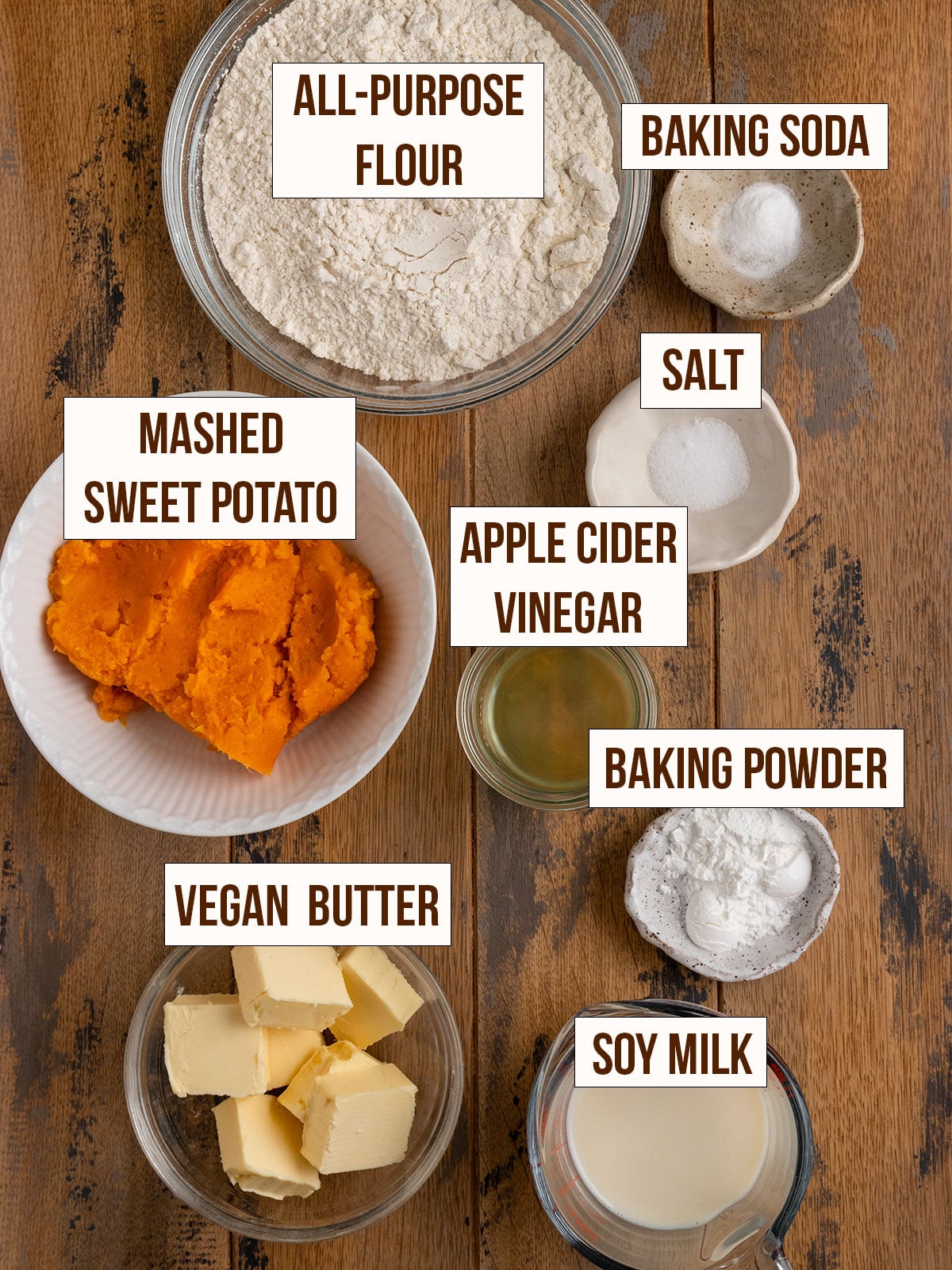 labeled ingredients for sweet potato biscuits including mashed sweet potato, flour, salt, baking powder, baking soda, soy milk, apple cider vinegar, and vegan butter.