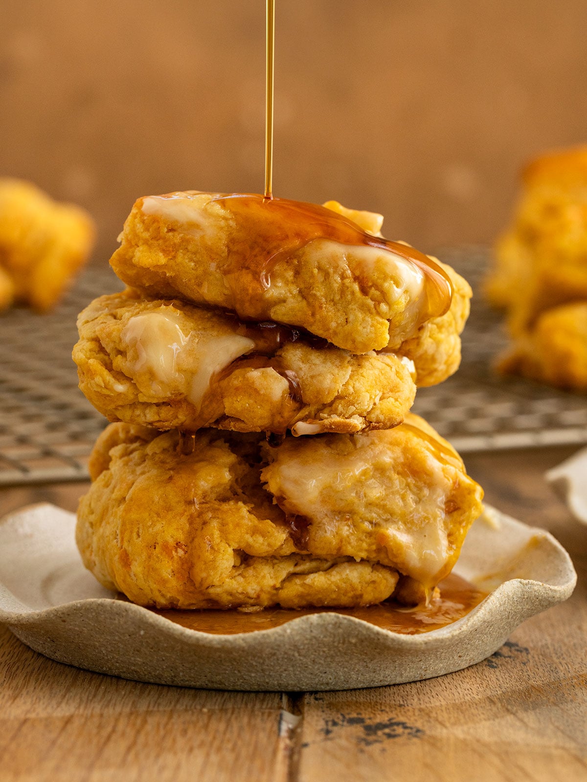 two sweet potato biscuits stacked on each other on a plate with butter on top and maple syrup being drizzled on top.