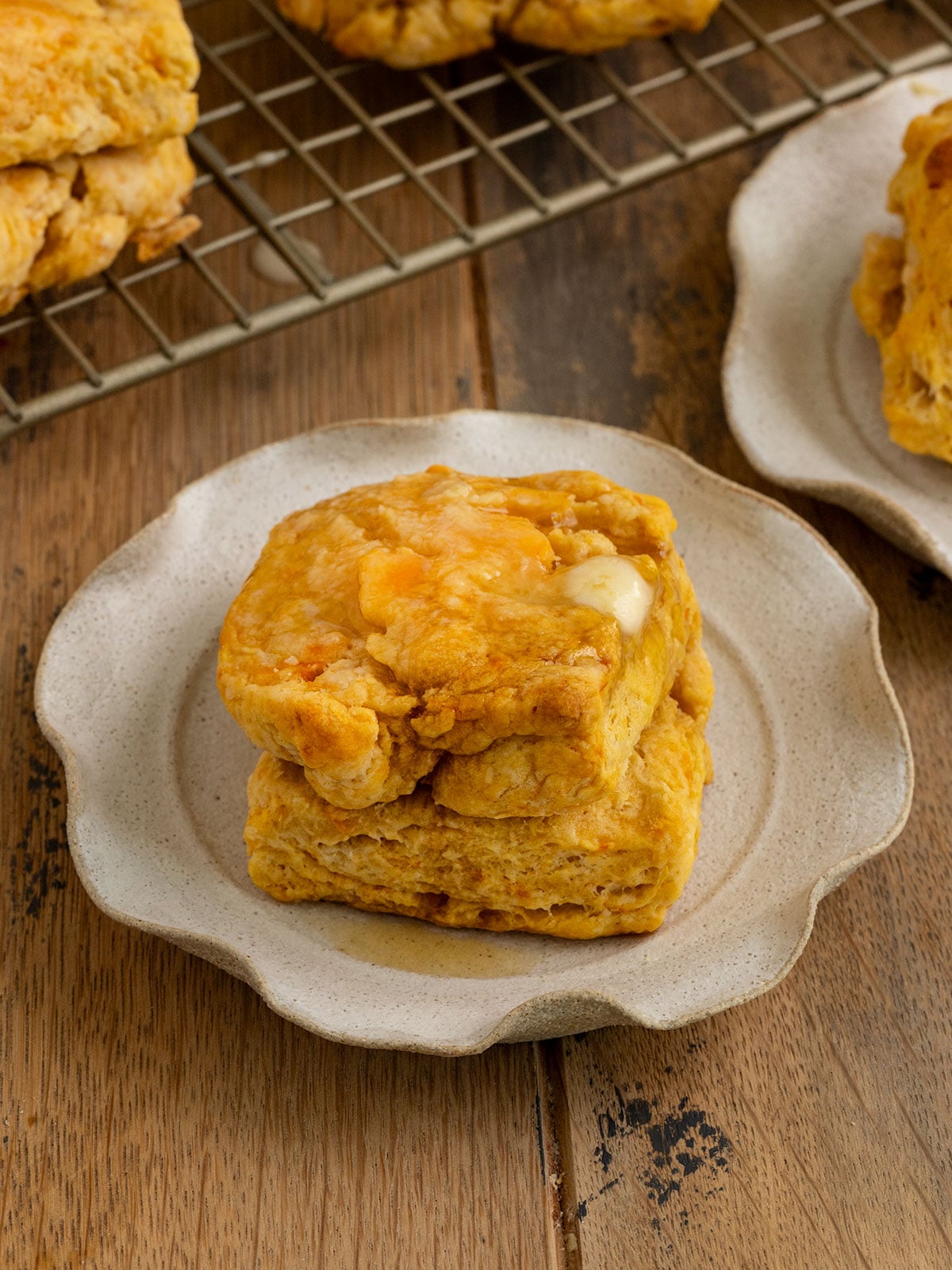 plate topped with a square orange sweet potato biscuit that is topped with melting butter.