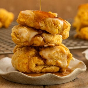 two sweet potato biscuits stacked on each other on a plate with butter on top and maple syrup being drizzled on top.