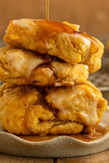 two sweet potato biscuits stacked on each other on a plate with butter on top and maple syrup being drizzled on top.